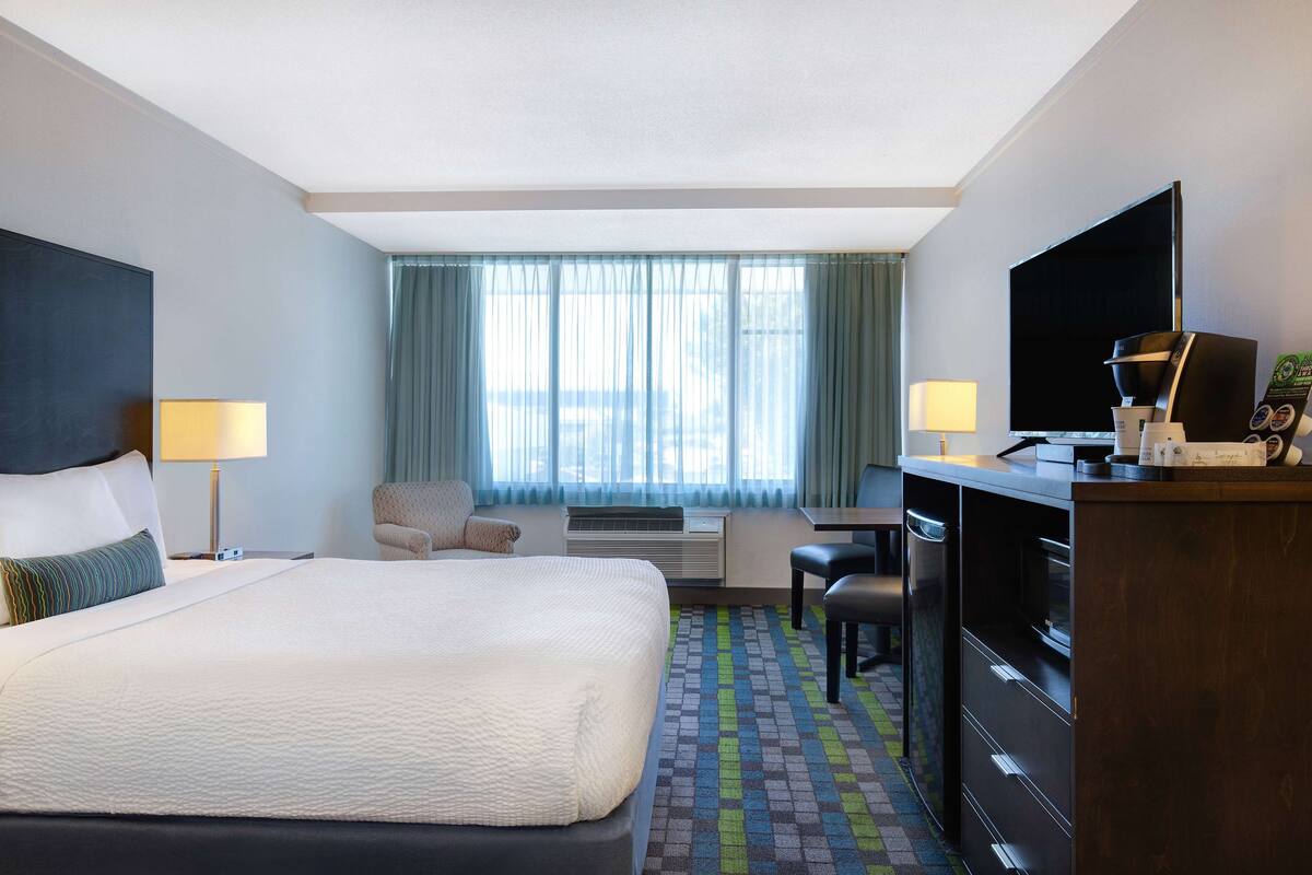 Ein Hotelzimmer mit einem großen Bett, einem Schreibtisch mit Computer, einem Fernseher und einer Kaffeemaschine.