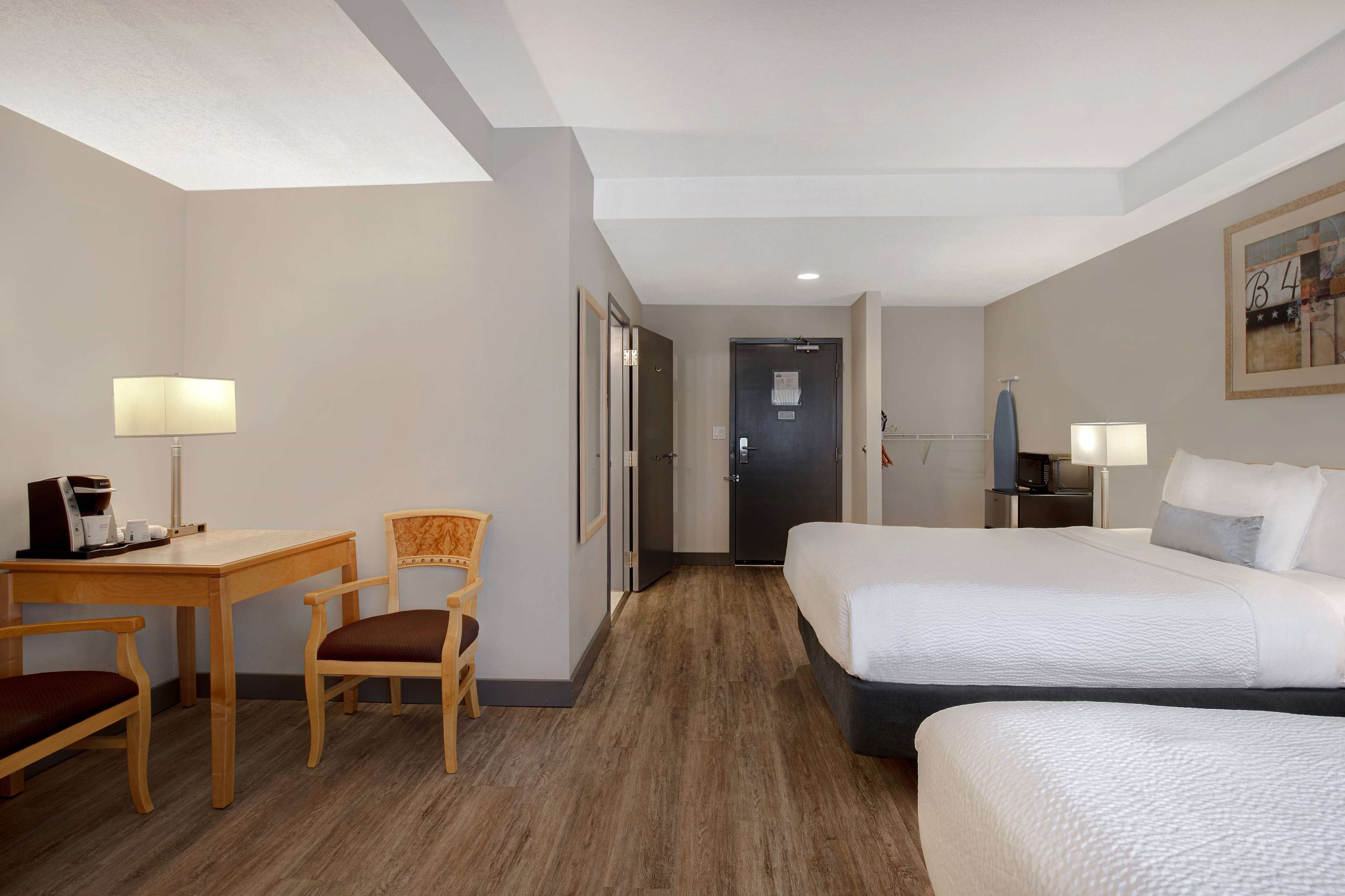 A hotel room with a bed, a desk with a coffee maker, a chair, and a door.