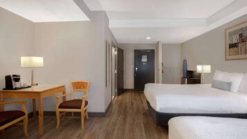 A hotel room with a bed, a desk with a coffee maker, a chair, and a door.