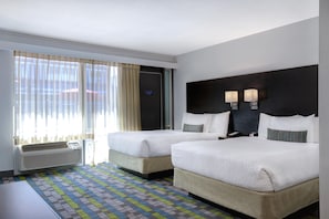 Habitación de hotel con dos camas, un ventanal con cortinas, aire acondicionado de pared y alfombra estampada.