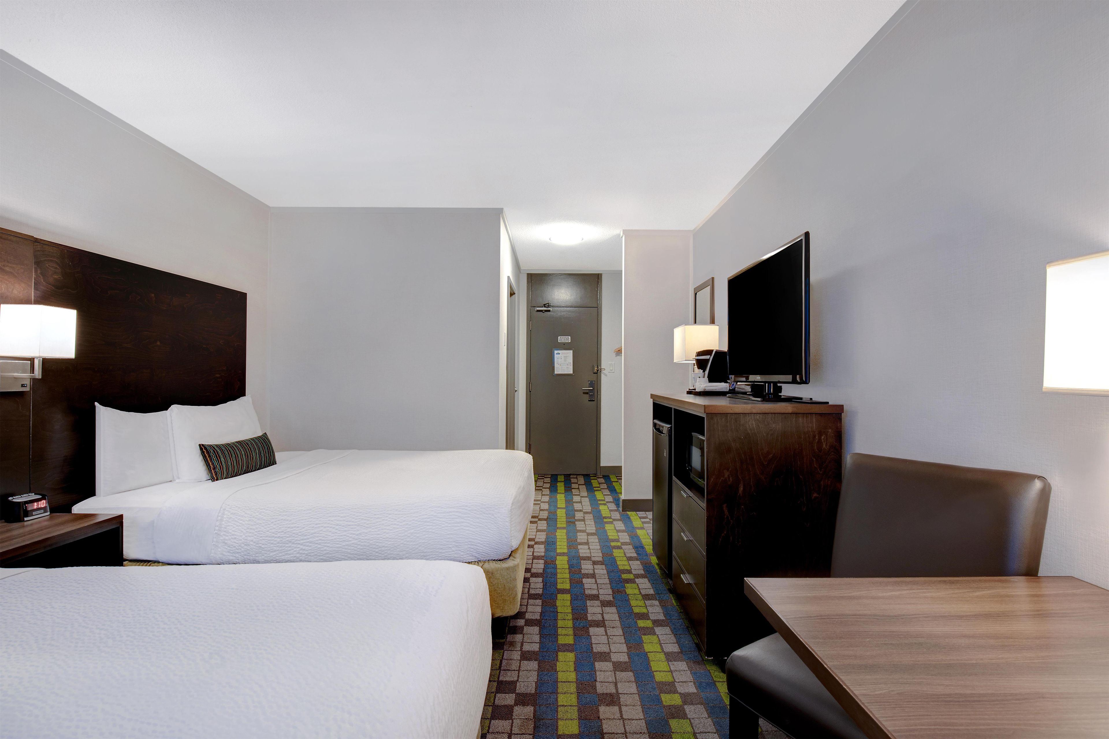 A hotel room with two beds, a desk, a television, and a bathroom visible in the background.
