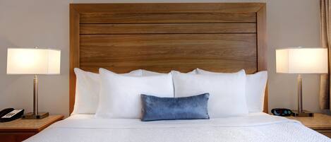 A hotel room with a large bed, two bedside lamps, a bedside phone, and a digital clock.