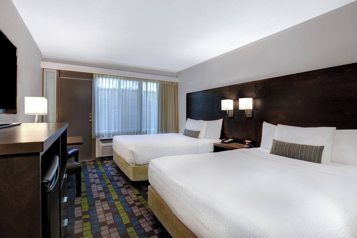 Ein Hotelzimmer mit zwei Betten, einem Schreibtisch, einem Sessel, einem Fernseher und einem Fenster mit Vorhängen.