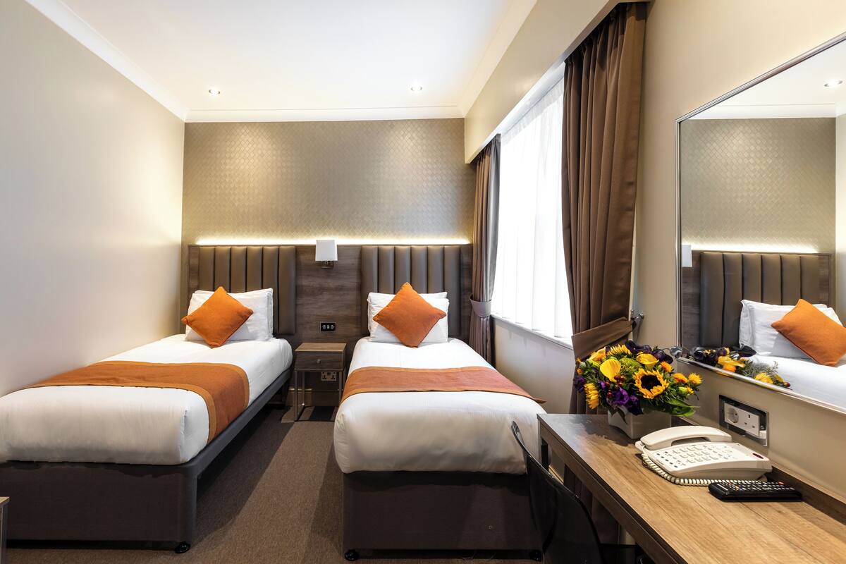A hotel room with two beds, a desk with a telephone, and a mirror.