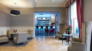 A lobby with a bar area, seating arrangements, and a decorative vase with flowers. - Sidney Hotel London Victoria  (London)