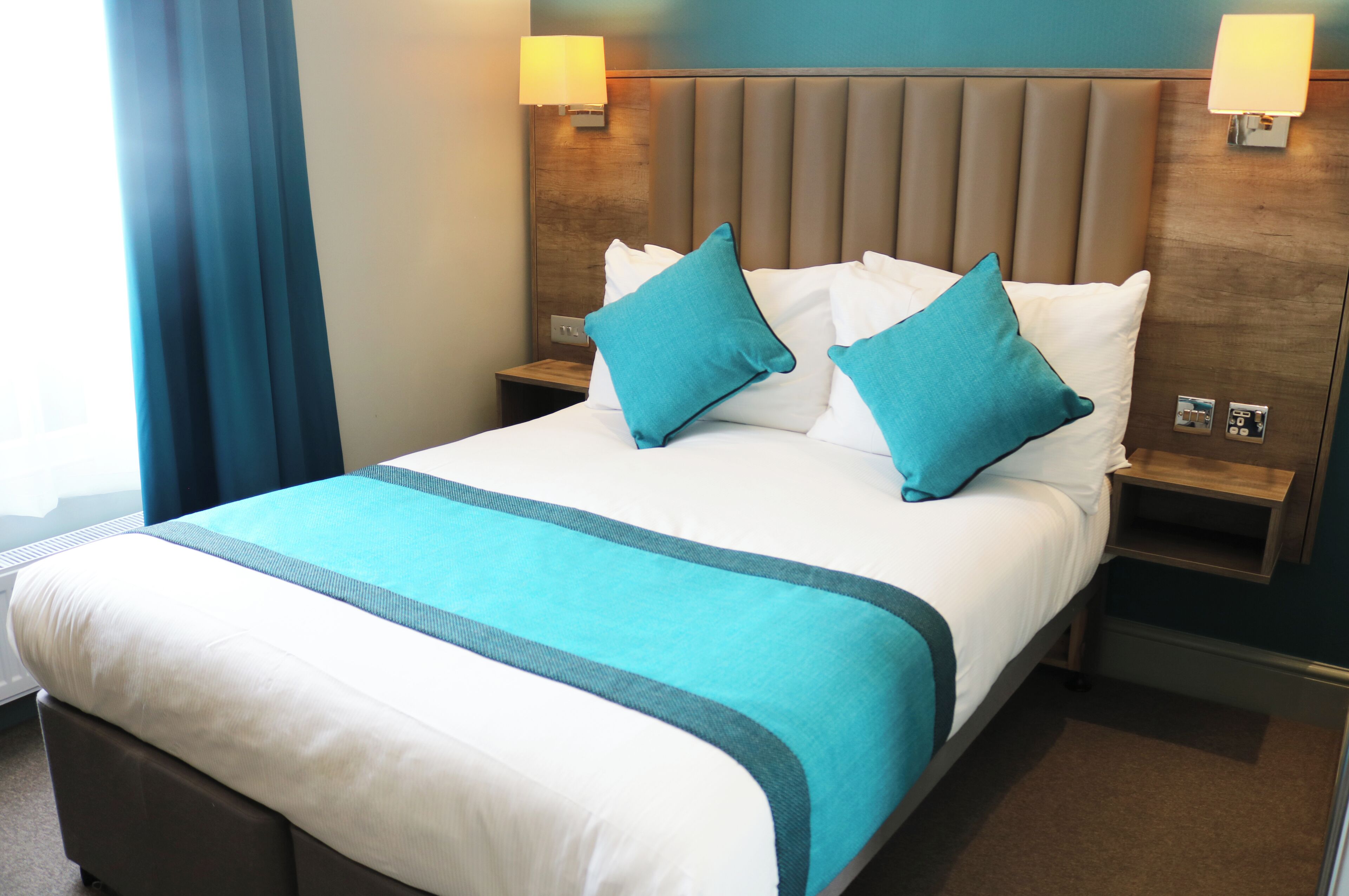 Een hotelkamer met een groot bed, twee nachtkastjes, een hoofdeinde en een raam met gordijnen.
