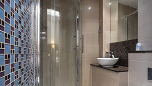 A modern bathroom with a glass-enclosed shower, a white sink, and a tiled backsplash. - Sidney Hotel London Victoria  (London)