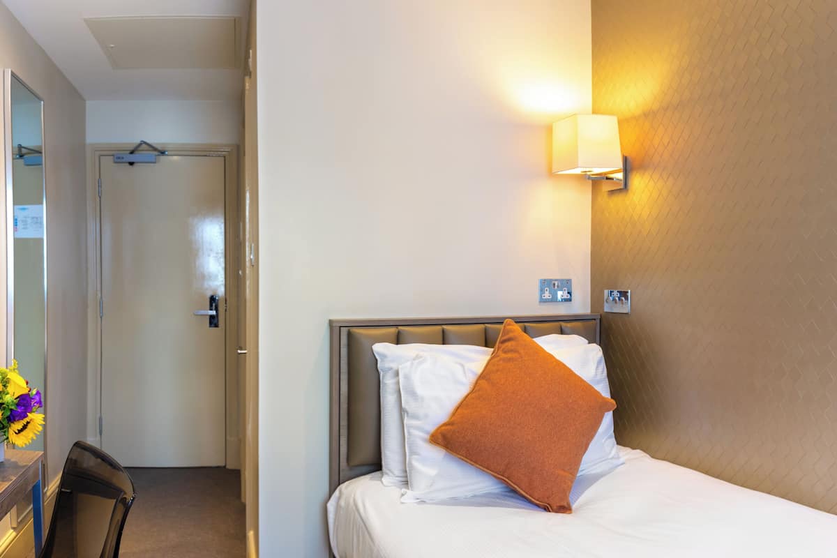 A hotel room with a bed, a nightstand, a lamp, and a door.