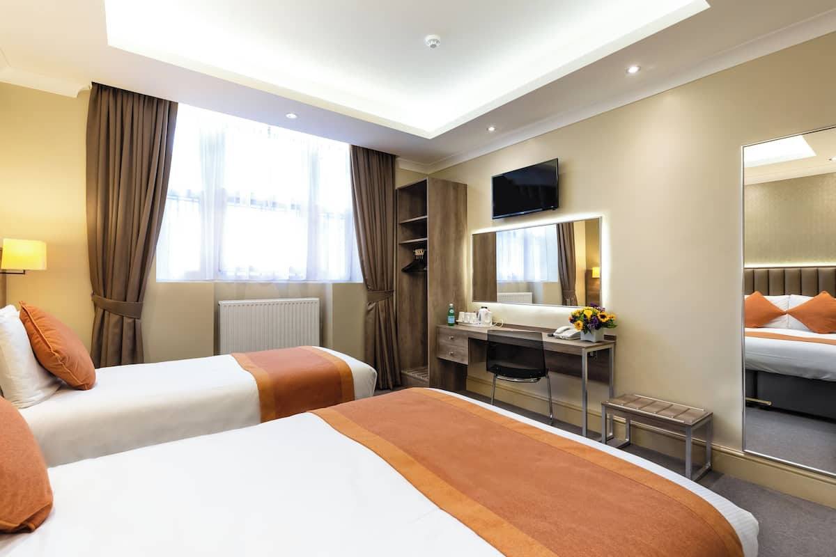 A hotel room with two beds, a desk, a chair, a mirror, a TV, and a window with curtains.