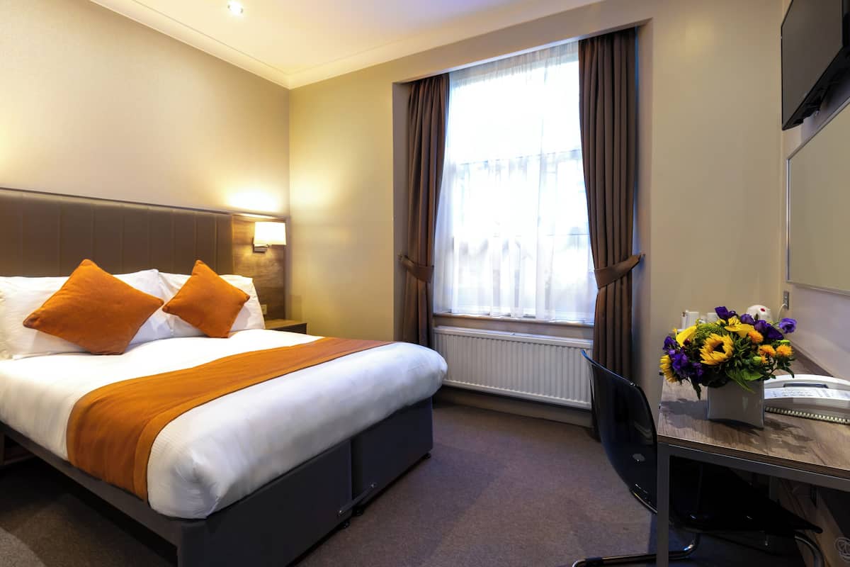 A hotel room with a bed, a desk with a telephone, and a window with curtains.