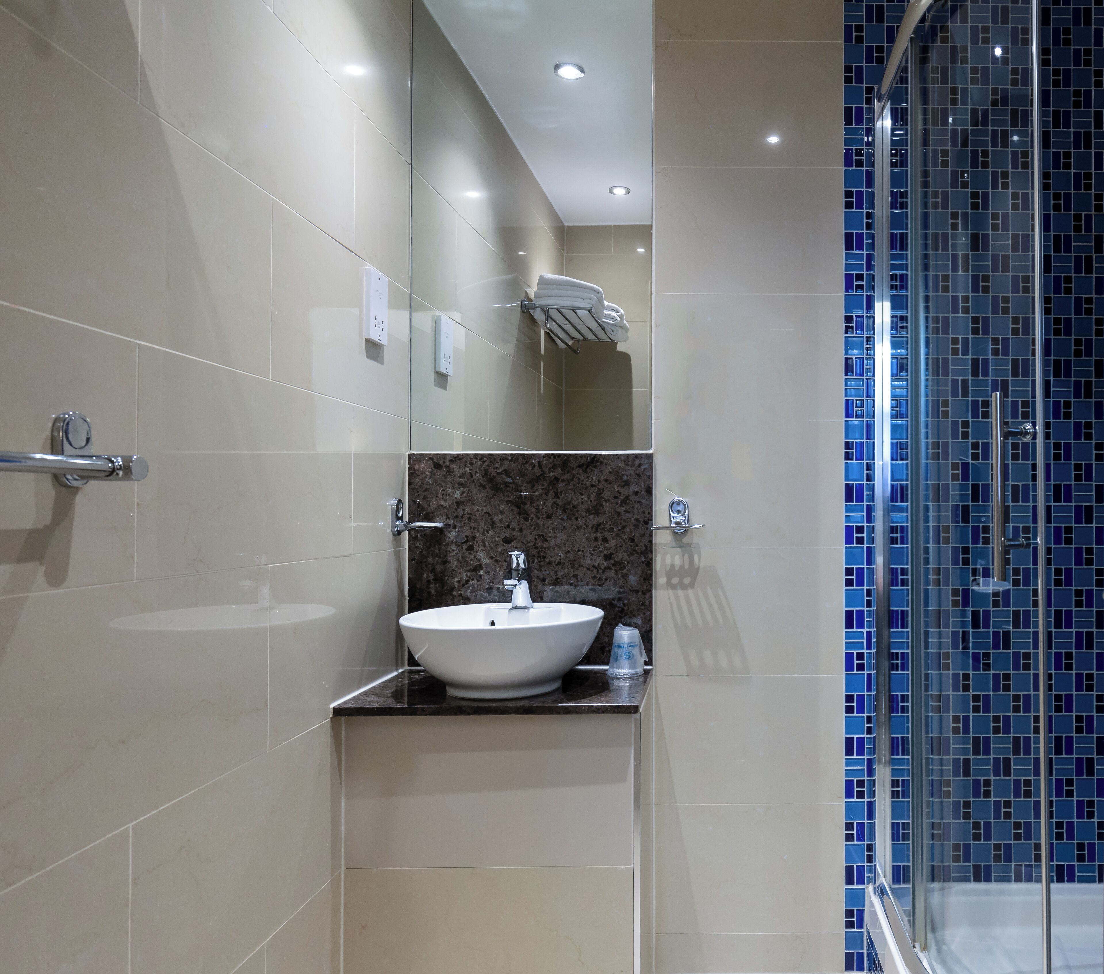 Un baño moderno con un lavamanos grande de color blanco, encimera de mármol y cabina de ducha de vidrio con mosaicos azules.