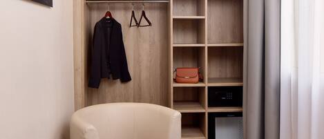 A modern hotel room with a comfortable chair, a small table, a wardrobe, and a television.