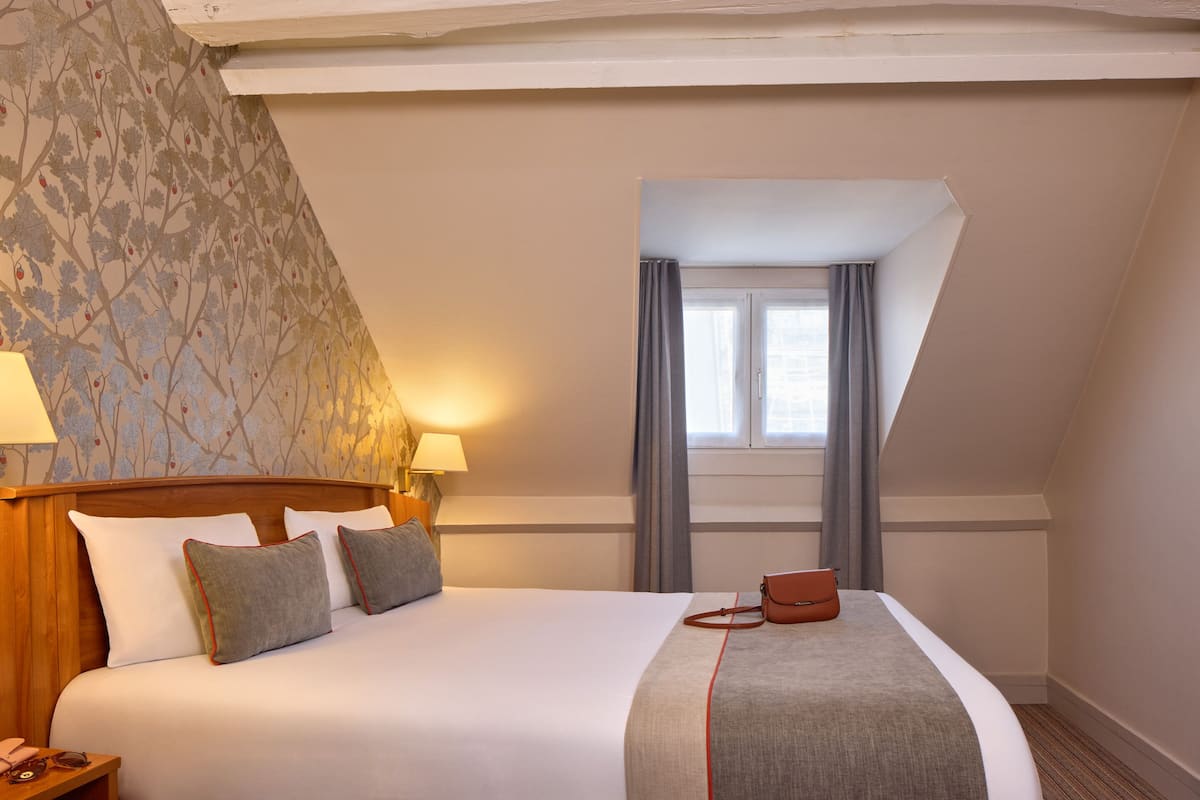 Hotellihuone, jossa on suuri sänky, kaksi yöpöytävalaisinta, ikkuna verhoilla ja puinen pääty.