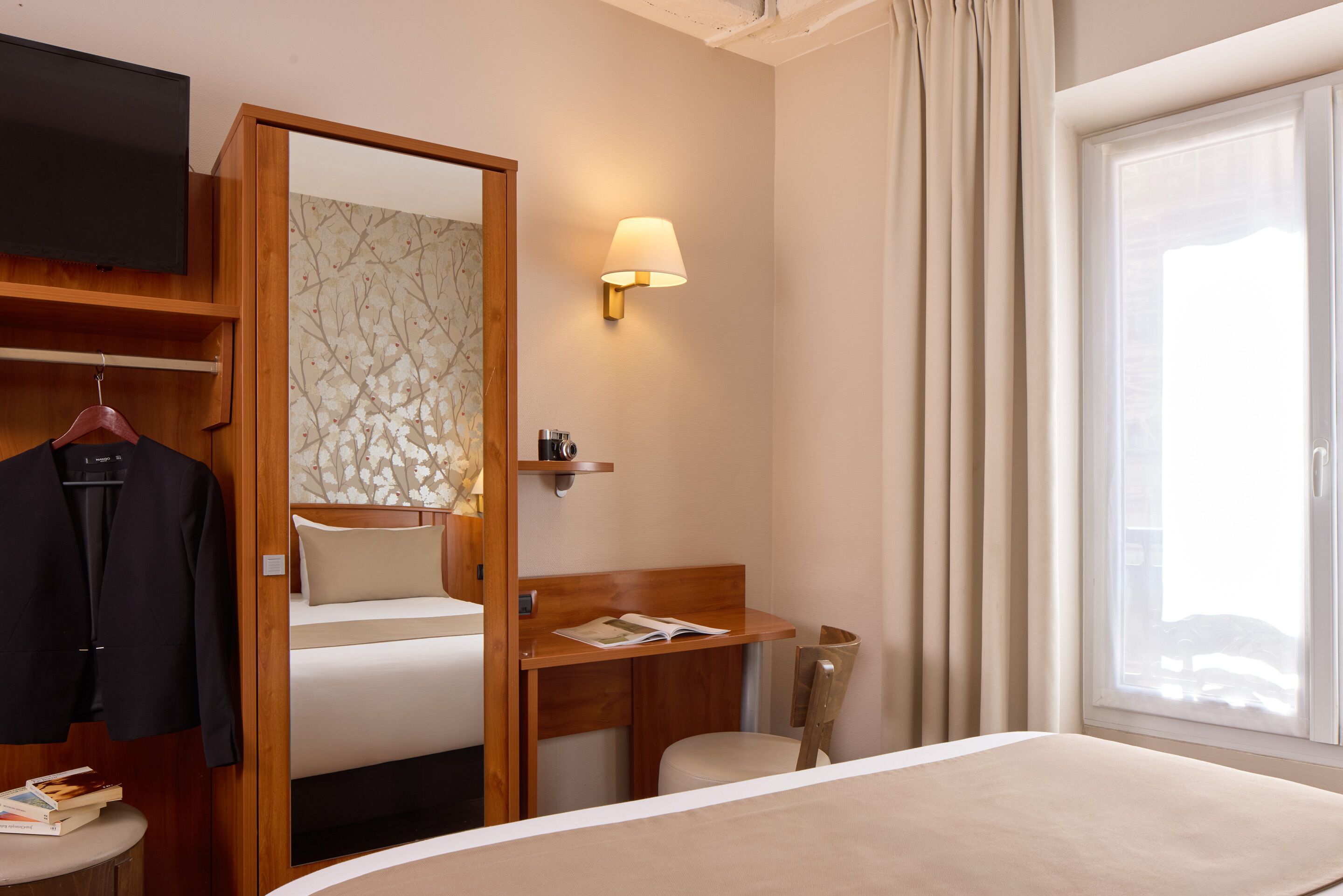 A hotel room with a bed, a desk, a chair, a TV, and a window with curtains.