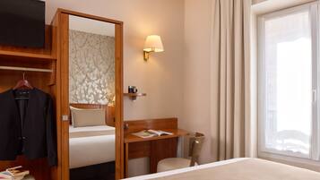 A hotel room with a bed, a desk, a chair, a TV, and a window with curtains.