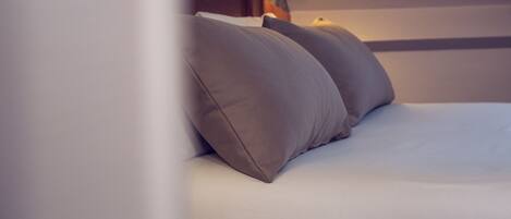 A neatly made bed with two pillows and a wall-mounted lamp.