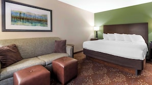 A hotel room with a bed, a sofa, an ottoman, a nightstand, a lamp, and a framed picture on the wall. - Best Western Plus New Ulm (New Ulm)