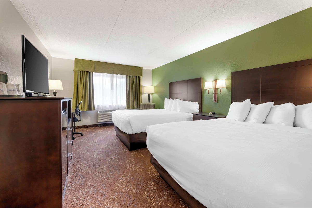 A hotel room with two beds, a desk with a TV, and a window with curtains.