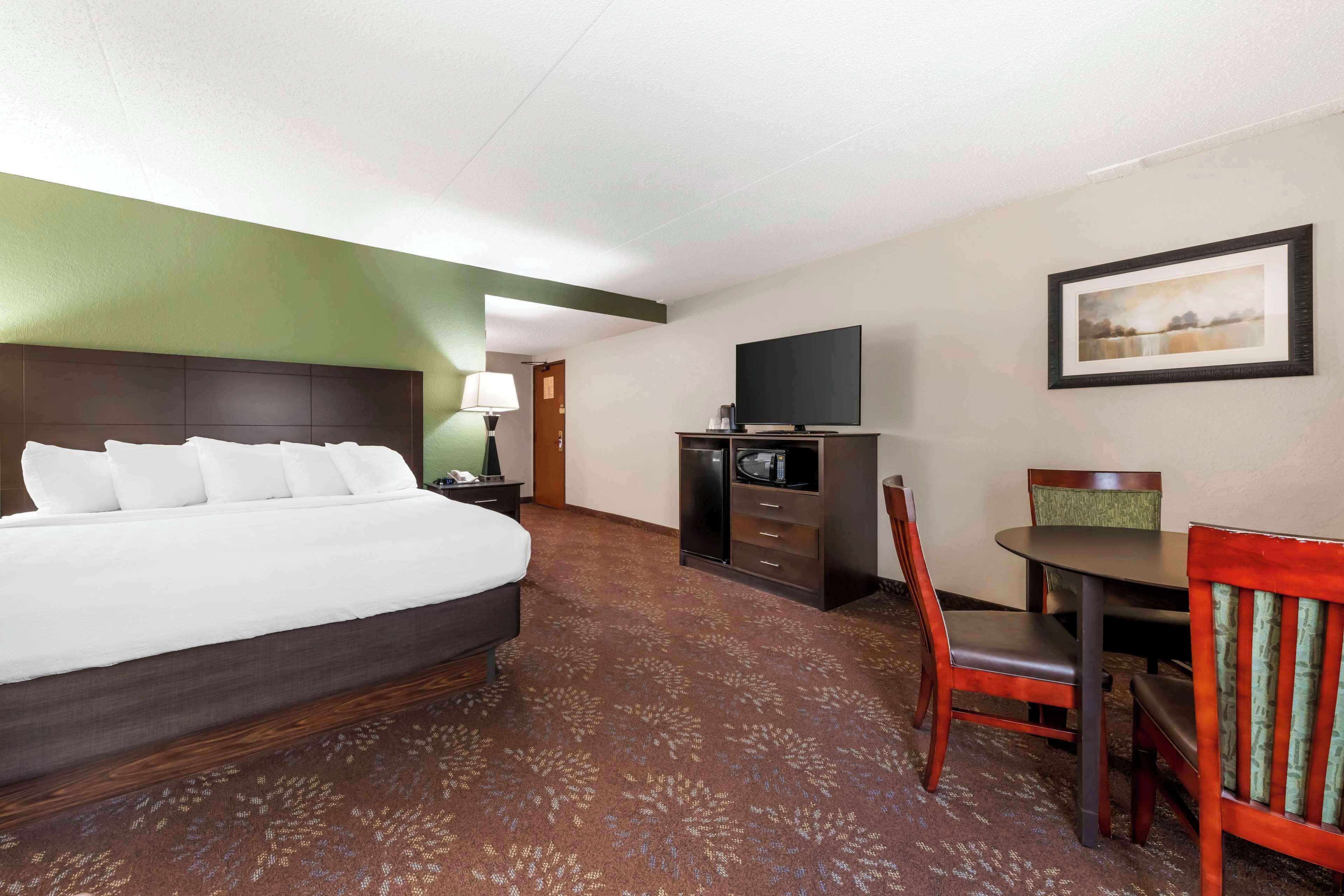 A hotel room with a bed, a desk, a chair, a television, and a framed picture on the wall.