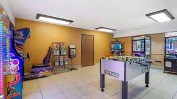 Une pièce avec un baby-foot marqué du nom « TORNADO », des jeux d’arcade et un vélo d’exercice violet.