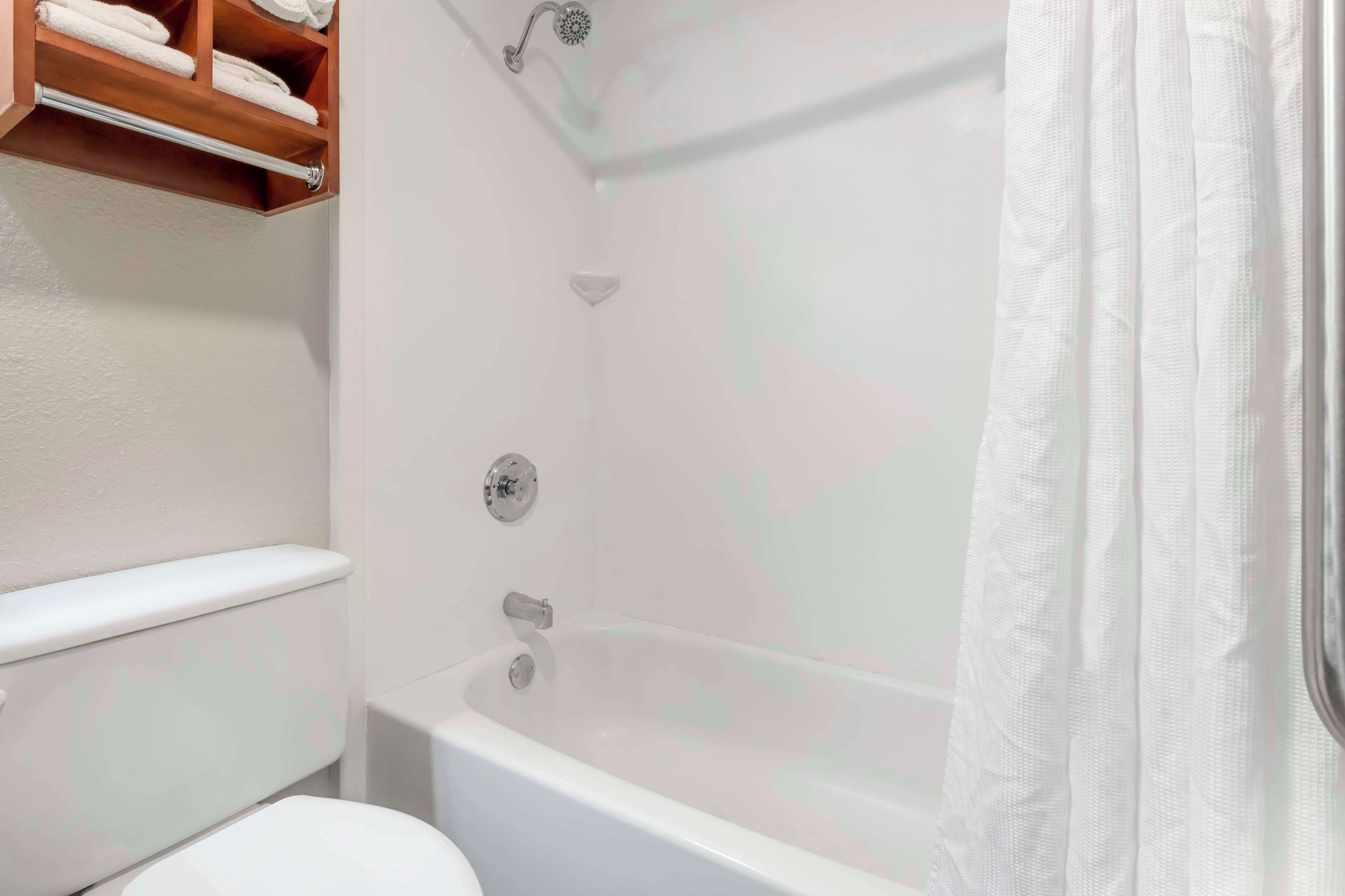 A bathroom with a white bathtub, a toilet, and a shelf with towels.