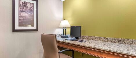 Ein Hotelzimmer mit Schreibtisch, Stuhl, Computer, Lampe und einem gerahmten Bild an der Wand.