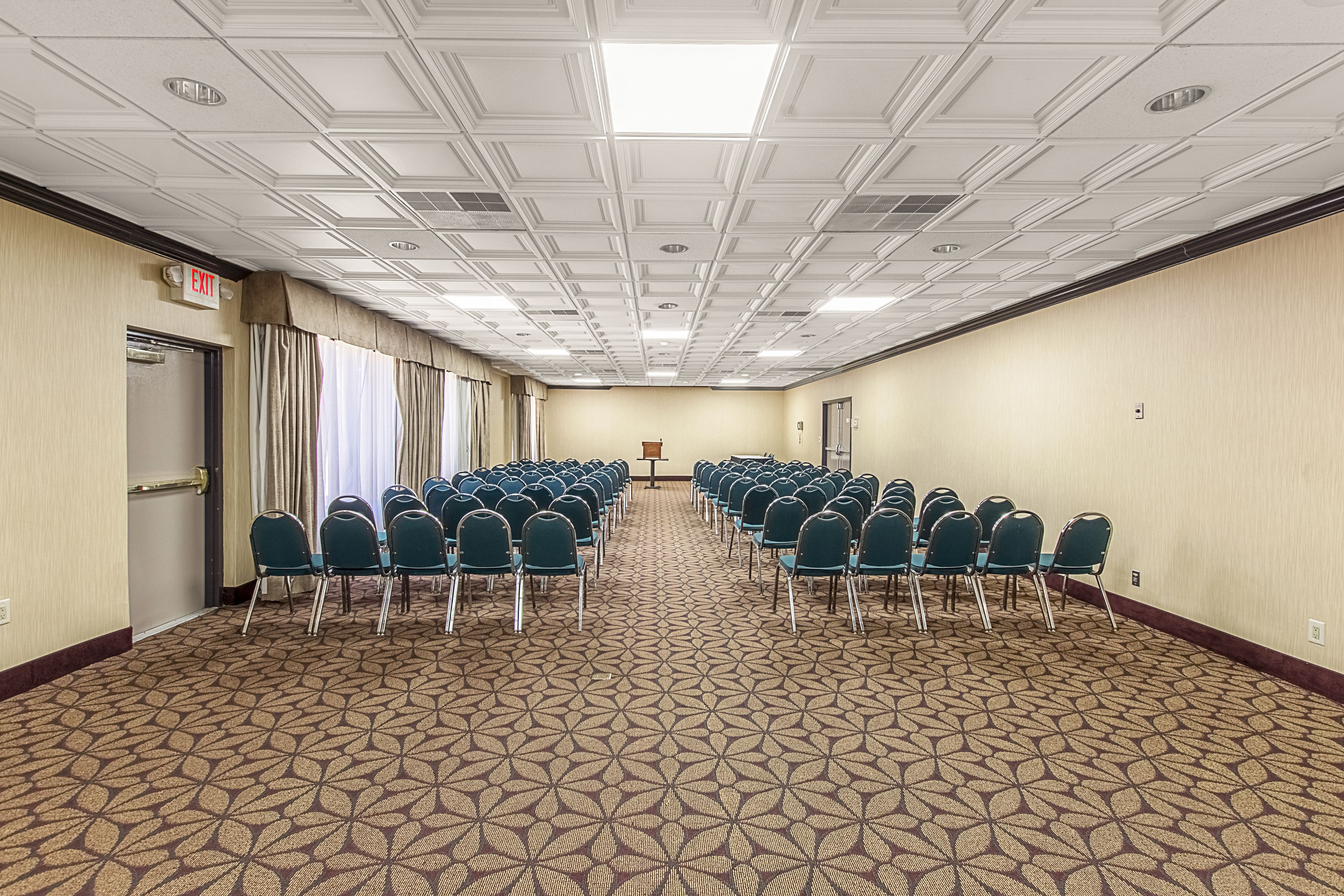 Une salle de conférence avec des rangées de chaises, un pupitre et un panneau indiquant la sortie.