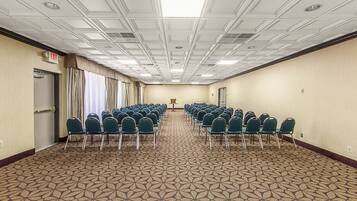 Une salle de conférence avec des rangées de chaises, un pupitre et un panneau indiquant la sortie.