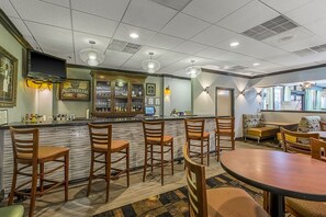 A bar area with wooden chairs, a counter with a computer, and a seating area with a sofa and chairs. - Clarion Inn Columbia Airport (West Columbia)