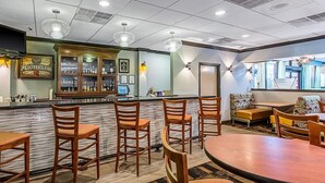 A restaurant with wooden chairs and tables, a bar area with a minibar, and a seating area with a sofa and cushions.