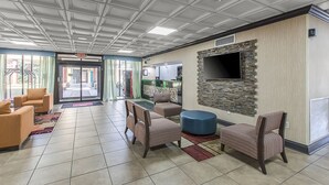 A lobby with a tiled floor, seating area with chairs and ottomans, a stone accent wall with a flat-screen TV, and a door marked "EXIT".