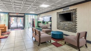 A spacious lobby with a tiled floor, striped armchairs, a blue ottoman, and a flat-screen TV mounted on a stone wall.
