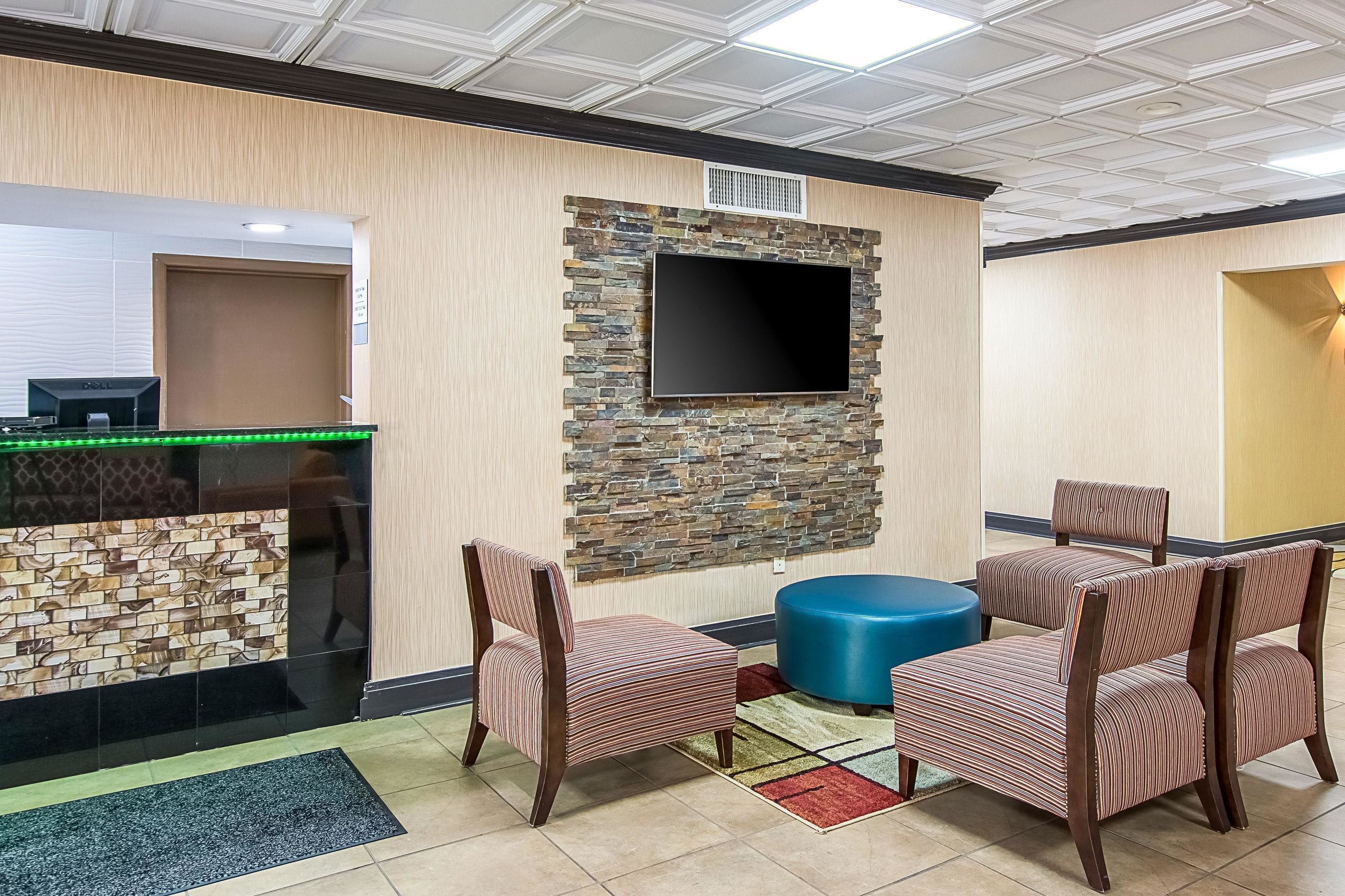 Un vestíbulo con mostrador de recepción, un televisor de pantalla plana montado en una pared de piedra y dos sillones a rayas con un reposapiés azul.