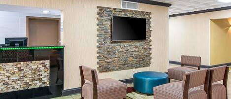 Un vestíbulo con mostrador de recepción, un televisor de pantalla plana montado en una pared de piedra y dos sillones a rayas con un reposapiés azul.