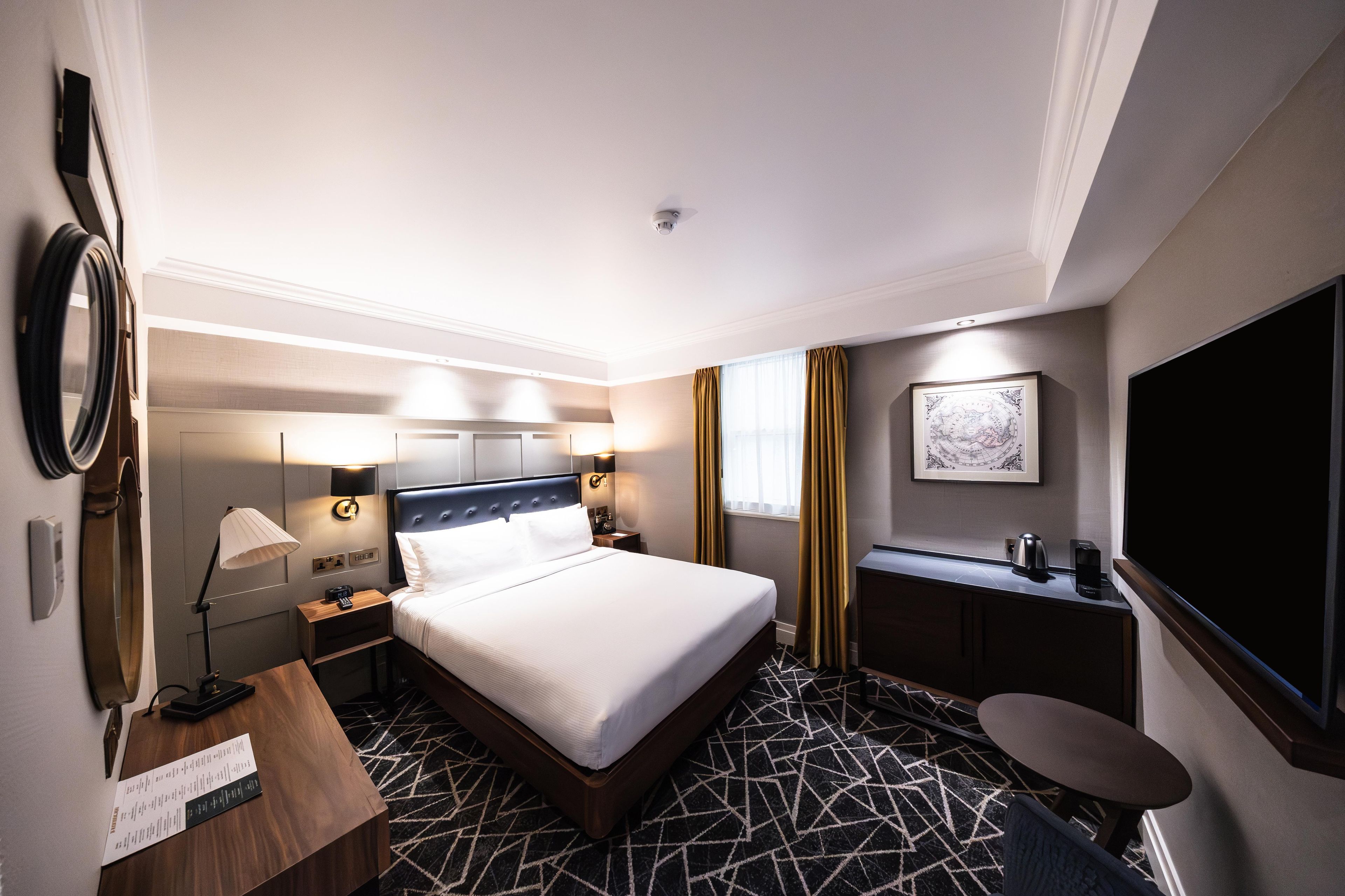 Ein Hotelzimmer mit Bett, Nachttischen, einem Schreibtisch, einem Sessel sowie einem Flachbildfernseher und einem wandmontierten Globus.