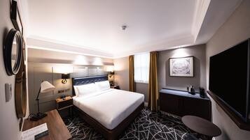 Ein Hotelzimmer mit Bett, Nachttischen, einem Schreibtisch, einem Sessel sowie einem Flachbildfernseher und einem wandmontierten Globus.