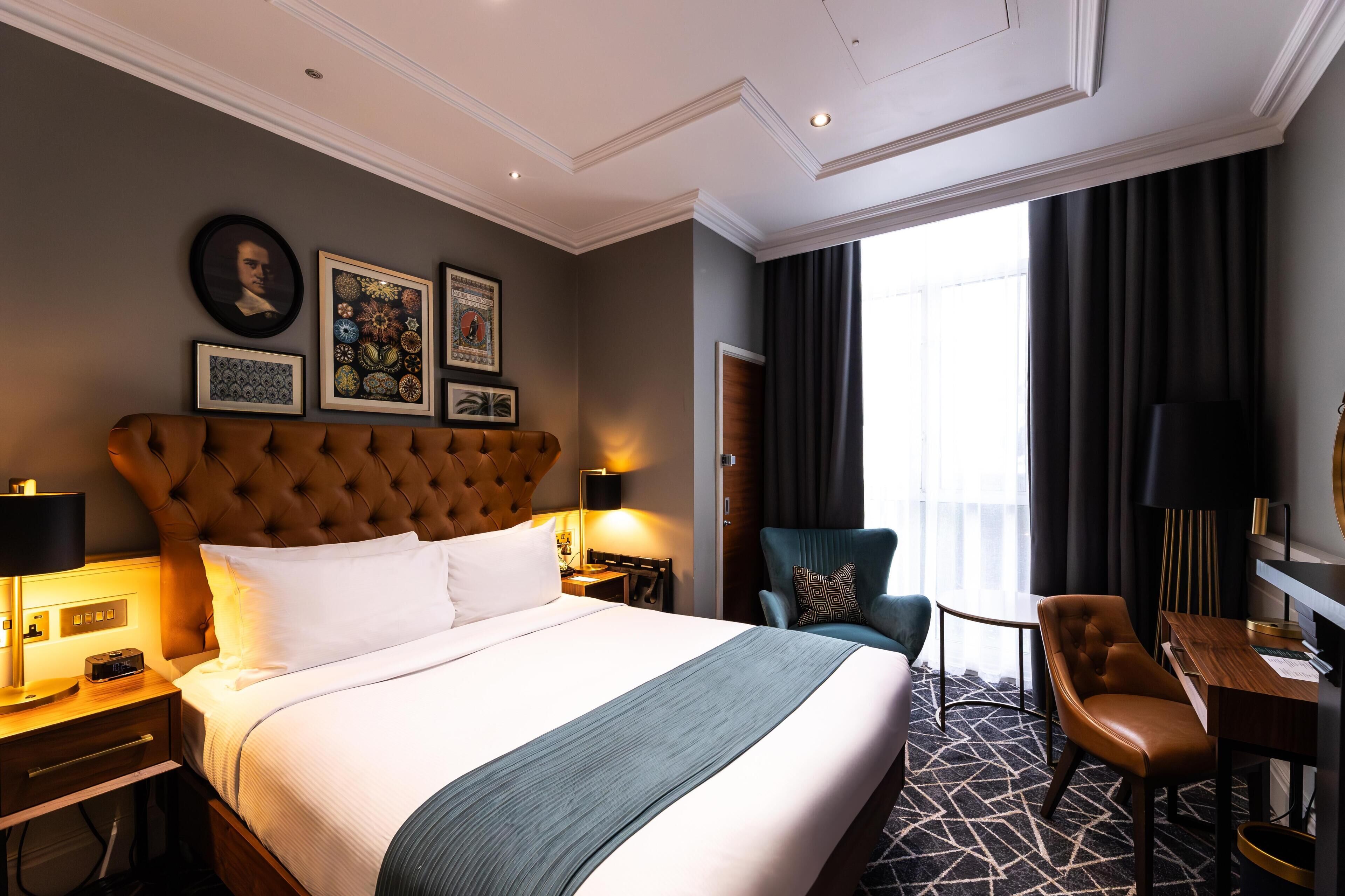 A hotel room with a large bed, a desk, a chair, and a view of the outdoors.