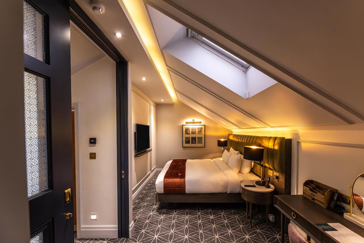 A hotel room with a skylight, a bed, bedside table, and a desk with a chair.