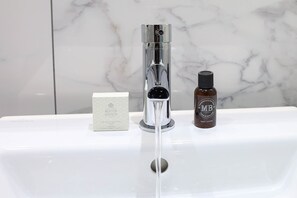 A bathroom sink with a chrome faucet, a bottle of body lotion, and a bar of soap. - 100 Queen's Gate Hotel London Kensington, Curio Collection by Hilton (London)