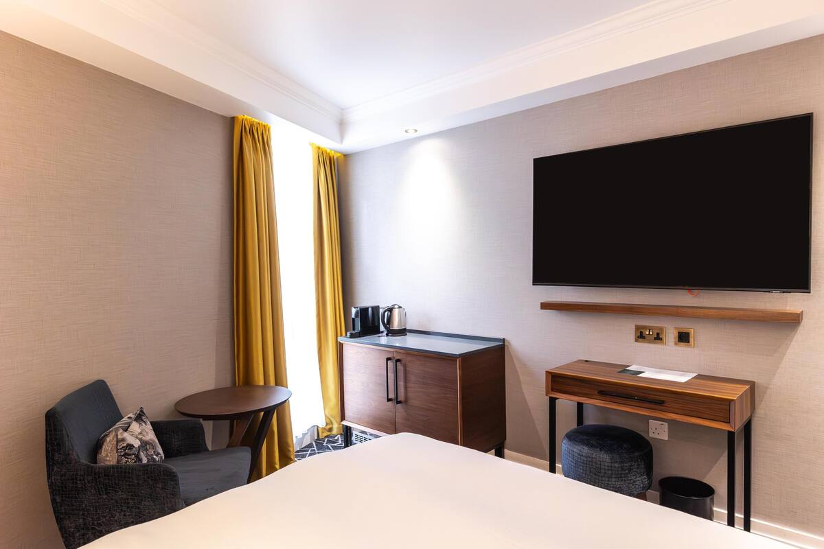A hotel room with a bed, a desk, a chair, a television, and a small table.
