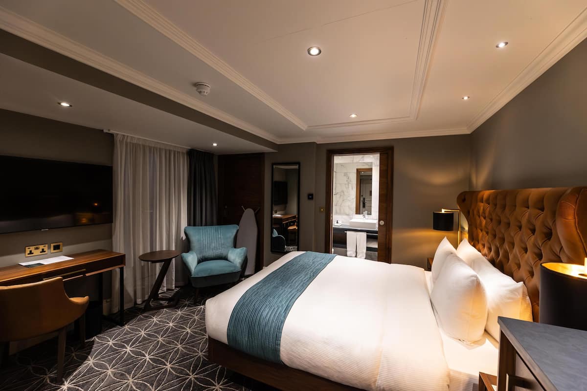 A hotel room with a bed, a desk, a chair, a TV, and a bathroom visible through an open door.