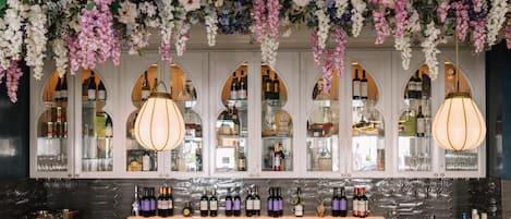 A bar area with a wine display, hanging floral decorations, and a modern light fixture.