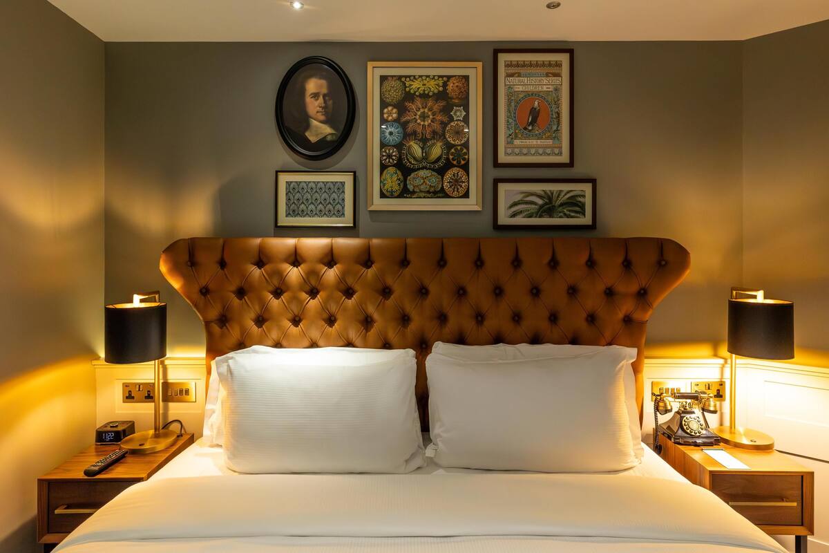 A neatly made bed with a tufted headboard, two bedside lamps, and framed pictures on the wall.