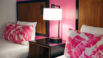 Habitación de hotel con dos camas, cada una con cabecero de madera, una mesita de noche con lámpara y pared rosa.