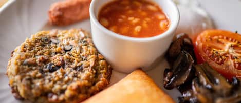 Un plato con un pastel horneado, un tazón de frijoles, una rodaja de tomate y una salchicha.