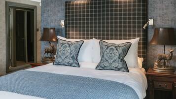 A neatly made bed with a blue blanket, two matching pillows, and a headboard with a plaid pattern. There are two nightstands with lamps and a deer statue on each.