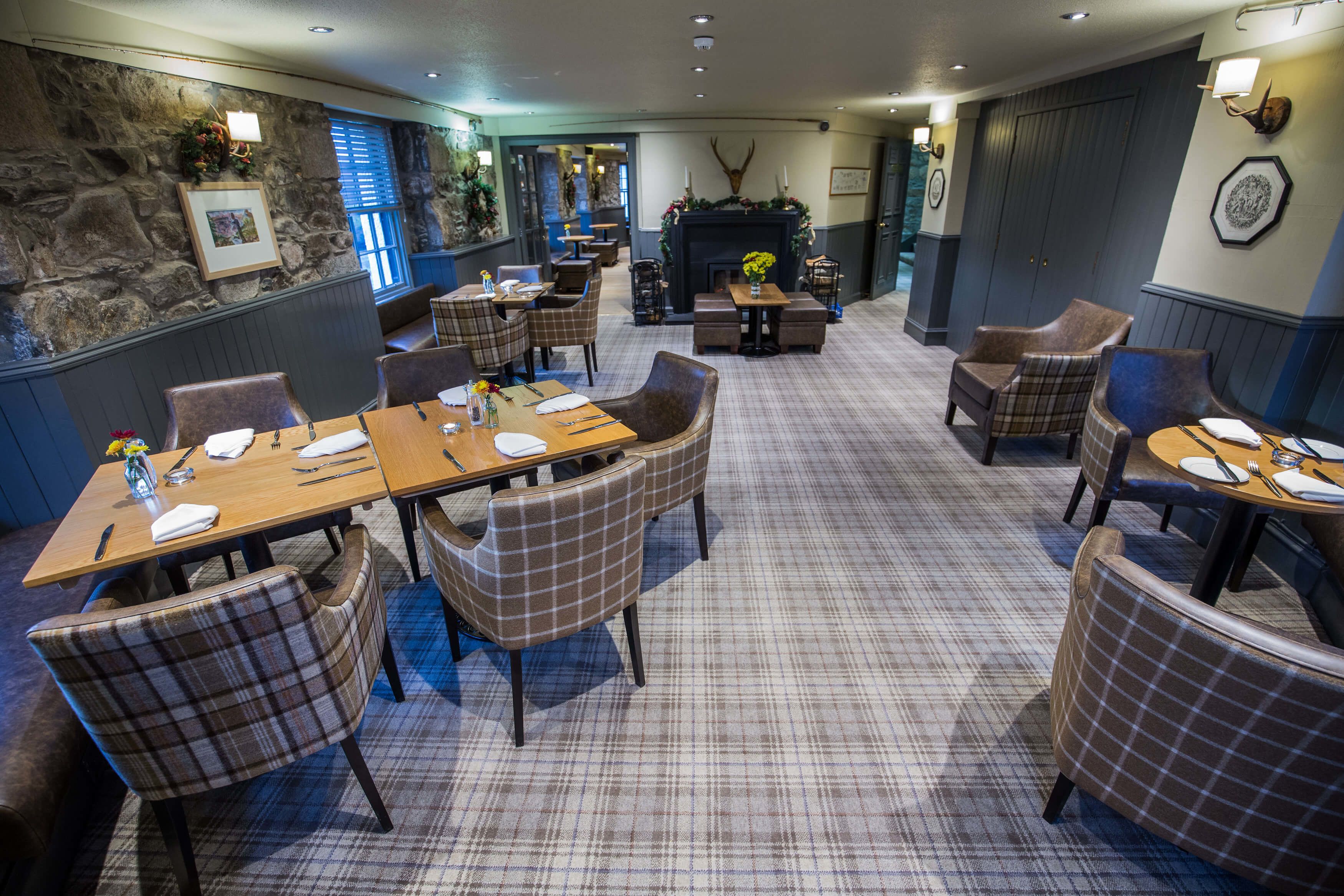 A restaurant with plaid-patterned chairs and tables, a stone wall, and a fireplace.