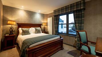 Habitación de hotel con una cama grande, dos mesitas de noche con lámparas, una silla, una ventana con vista a un coche y una cortina a cuadros.