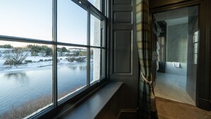 Une pièce dotée d’une grande fenêtre donnant sur un lac gelé, une salle de bain avec une douche en verre et une porte en bois sombre.
