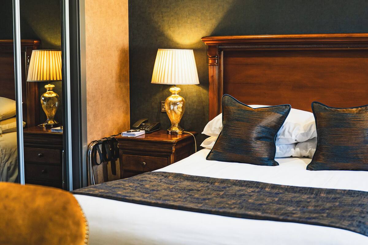Ein Hotelzimmer mit einem großen Bett, einem Holzkopfteil, einem Nachttisch mit Lampe und einem Sessel.